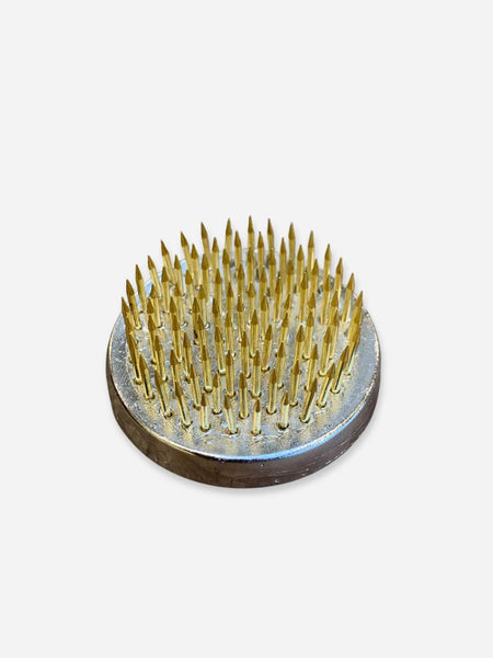 A circular metal spiked pad with numerous short, sharp metallic pins, photographed on a plain light gray background.