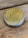 A round metal nail hammer with golden-yellow metal nails, resting on a rustic wooden surface.
