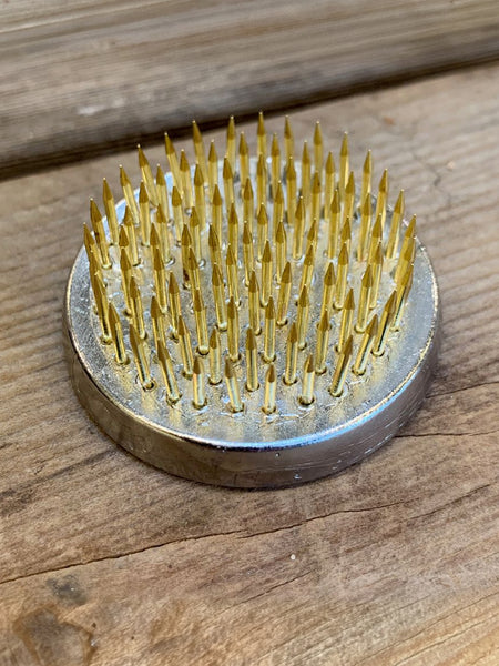 A round metal nail hammer with golden-yellow metal nails, resting on a rustic wooden surface.