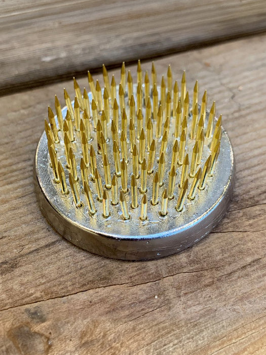 A round metal nail hammer with golden-yellow metal nails, resting on a rustic wooden surface.