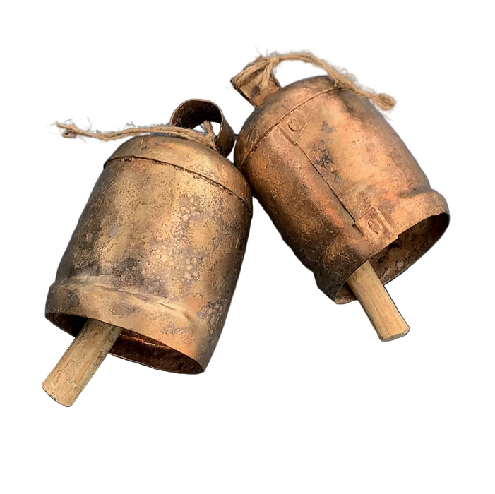 Two rustic antique metal bells with wooden mallets and jingles, displayed on a solid blue background.