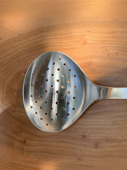 A stainless steel slotted spoon with a perforated bowl, shown on a warm-toned wooden surface.