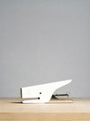 A minimalist white desk staple with a sleek, modern design resting on a light wood surface against a solid gray background.