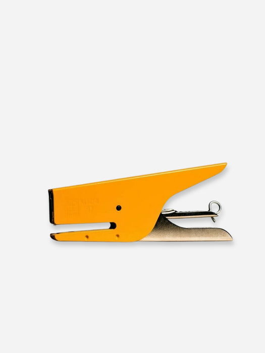 A bright yellow-orange metal staple with a silver-toned metal spring and a small black rubber tip, shown on a plain light gray background.