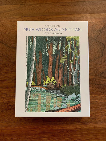 The front cover of the 'Muir Woods and Mt. Tam' note card box by Tom Killion, featuring a forest illustration, placed on a wooden surface.