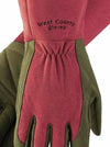 A close-up of a heavy-duty work glove with a dusty rose pink leather palm and fingers, olive green leather back and wrist, and black embroidered text reading 'West County gloves'.