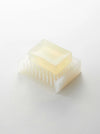 A translucent pale yellow rectangular bar of soap resting on a matching translucent white soap dish with vertical slots, photographed on a clean white background.